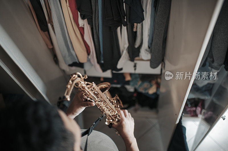 top view of asian chinese mid adult man practicing saxophone facing his wardrobe as soundproof to reduce the sounds disturbing his neighbor  in his apartment